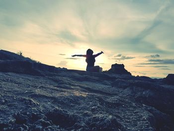 Silhouette man standing on rock by sea against sky during sunset