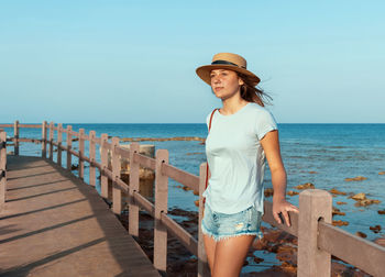 Teen girl standing on wooden walkway by the sea at sunset