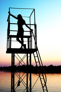 Silhouette man standing by lake against clear sky during sunset