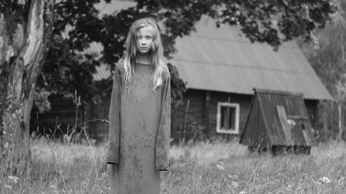 Portrait of girl standing on field against building