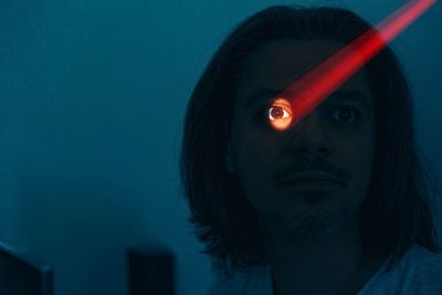 Portrait of young man with illuminated eye against blue background