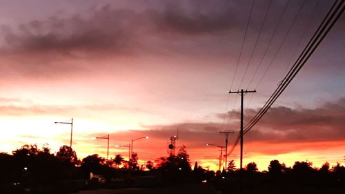 Low angle view of silhouette electricity pylon against dramatic sky