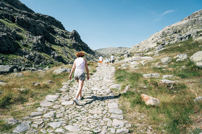 Rear view of people hiking on dirt road amidst rocky mountains