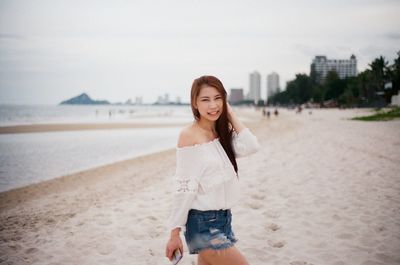 Portrait of young woman walking at beach against sky