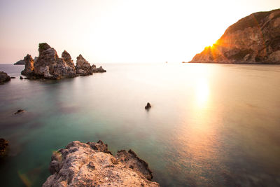 Rock formation in sea against sky during sunset