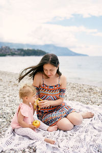 Happy woman sitting on shore at beach against sky