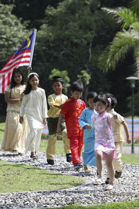 Friends in traditional clothing holding malaysia flag while walking on footpath