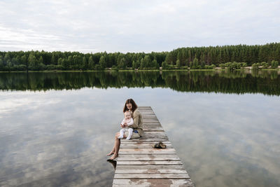 Mother spending leisure time with baby girl by lake on jetty