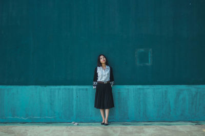 Full length of young woman standing against blue wall