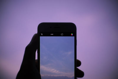 Low angle view of hand holding smart phone against sky