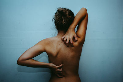 Rear view of shirtless woman standing against wall