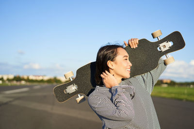 Side view of young woman standing against sky