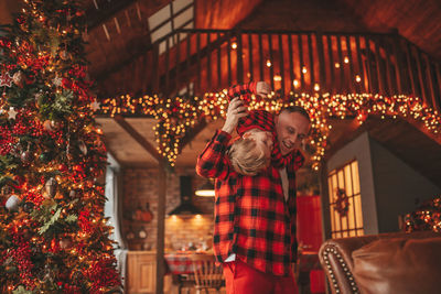 Candid authentic happy dad and son in red plaid pajamas fooling around at wood lodge xmas decorated