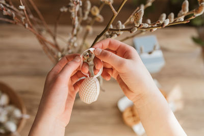  girl's hands hanging a decorative easter egg on a willow branch at home. decorating home for easter