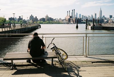 Rear view of man sitting on railing against river