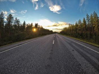 Empty road by trees against sky