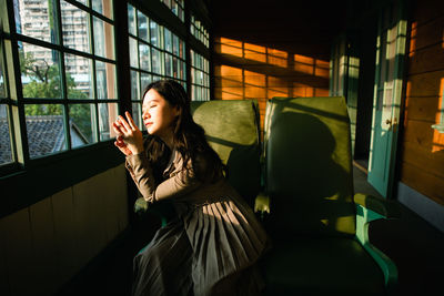 Young woman looking away while sitting in window