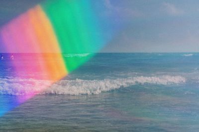 Digital composite image of rainbow over sea against sky