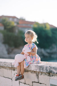 Side view of mother and daughter sitting on retaining wall