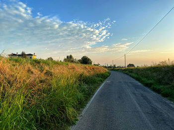 Road amidst field against sky during sunset