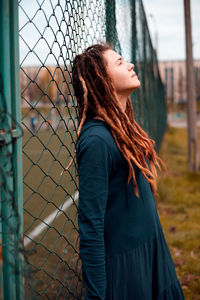 Young woman standing against chainlink fence