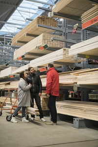 Customers and salesman standing by wooden planks on shelves in hardware store
