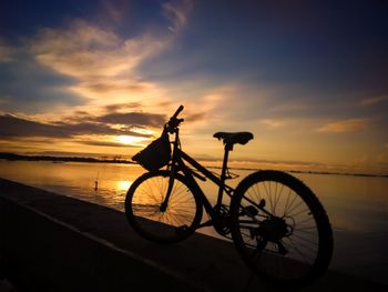 Bicycle on beach against sky during sunset
