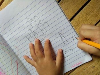 Cropped hands of child writing on book