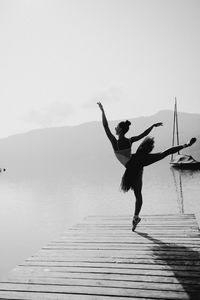 Ballet dancer dancing on pier over river against sky