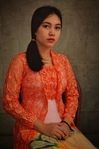 Portrait of beautiful young woman sitting on chair against wall