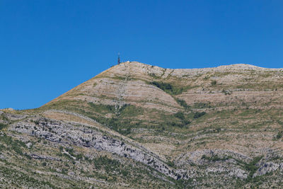 Low angle view of rocky mountain against clear blue sky