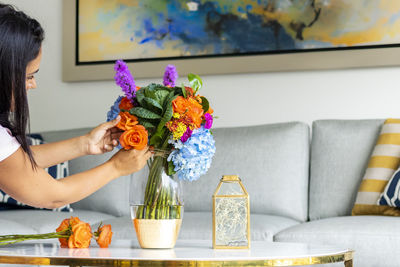 Woman arranging flowers in vase on table at home