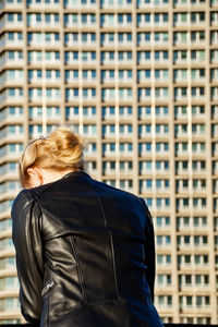 Rear view of woman wearing leather jacket while standing against building