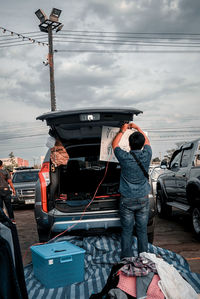 Rear view of man standing on car against sky