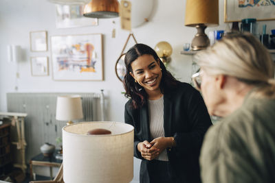 Smiling female owner with senior customer buying electric lamp at antique store