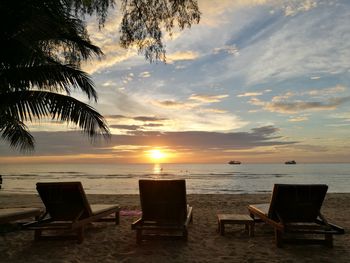 Chairs on beach against sky during sunset