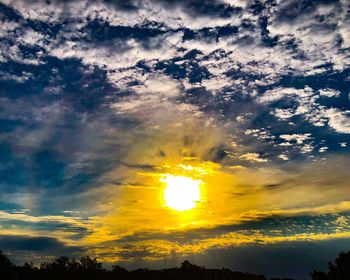 Low angle view of silhouette trees against dramatic sky during sunset
