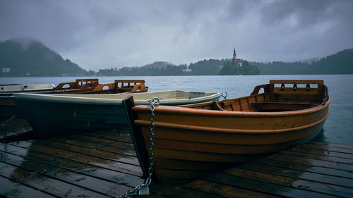 Boats moored on pier over lake against sky