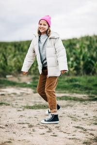 Cheerful beautiful teenage girl in a yellow raincoat and a pink hat is dancing on the background