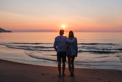 Rear view of couple standing on beach during sunset