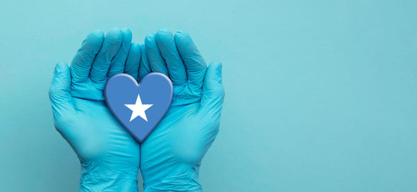 Close-up of hand holding heart shape against blue background