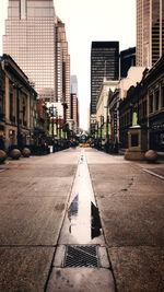 Empty road amidst buildings in city against sky