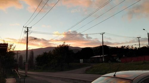 Road by electricity pylon against sky during sunset