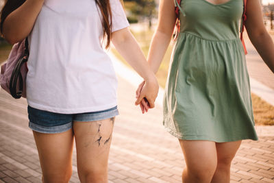 Midsection of lesbian couple holding hands while walking in city