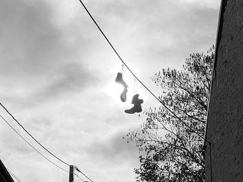 Low angle view of silhouette man hanging on rope against sky