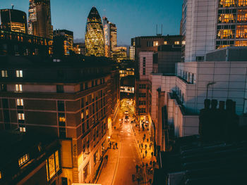 Illuminated city street amidst buildings by 30 st mary axe at dusk