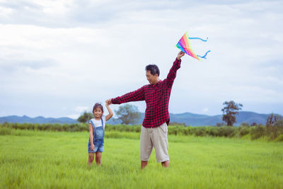 Man holding kite while standing with daughter on grassy field