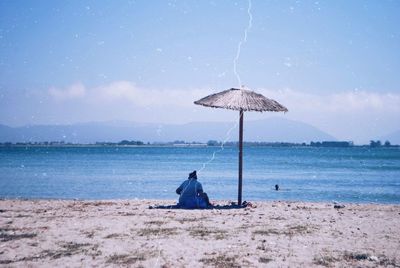 Rear view of men sitting on beach against sky