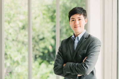 Portrait of smiling young businessman with arms crossed standing in office