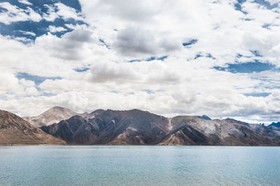 Scenic view of pangong lake by mountains against cloudy sky